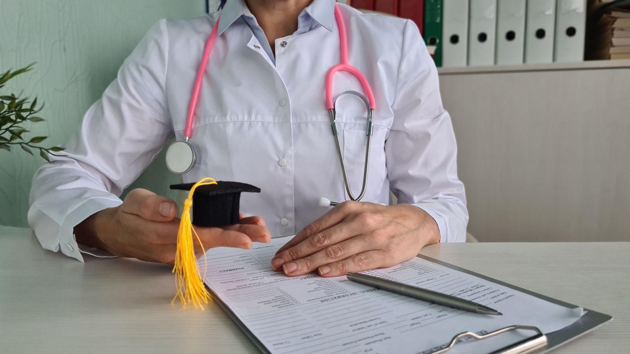 A doctor with stethoscope and a graduation cap on a clipboard, marking the transition from medical school to residency