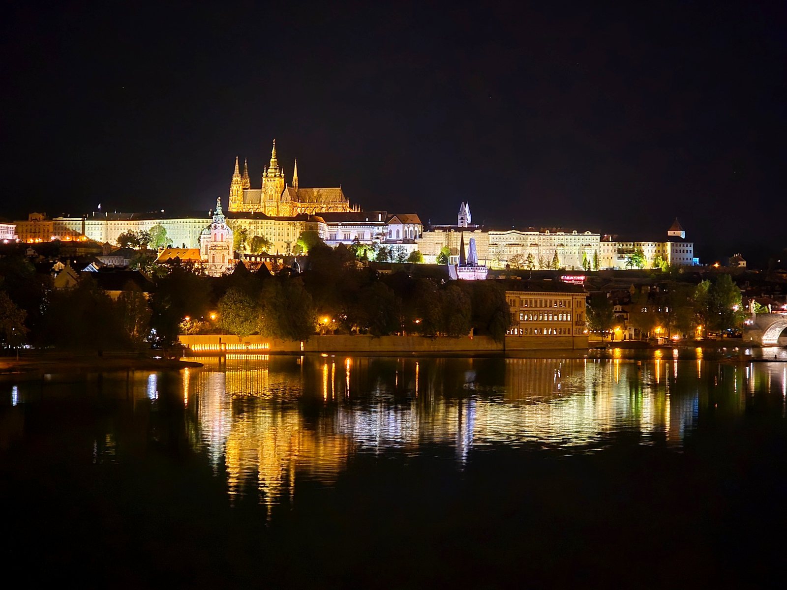 Prague Castle and St. Vitus Cathedral lit at night, reflected in the Vltava river